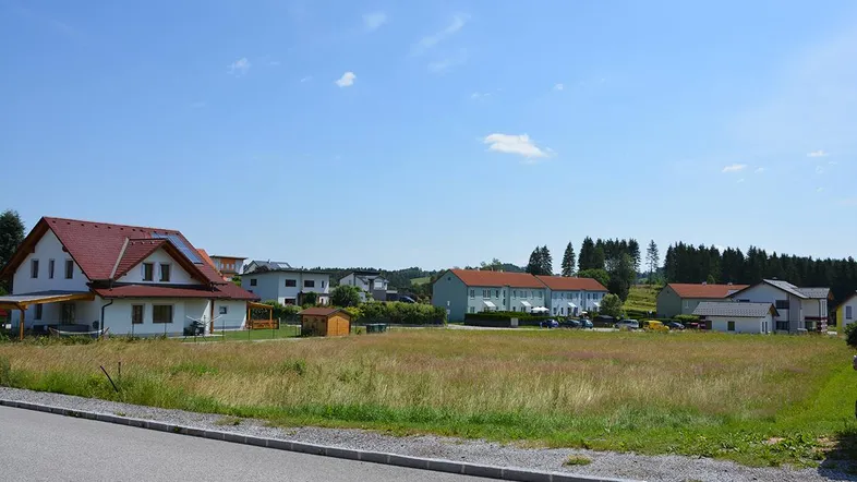Weitläufige Landschaft mit Wohnhäusern und einem großen Feld unter blauem Himmel.