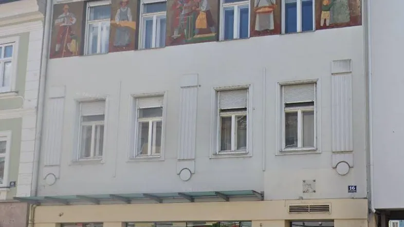 Historisches Gebäude mit bemalter Fassade und Geschäftsräumen im Erdgeschoss.