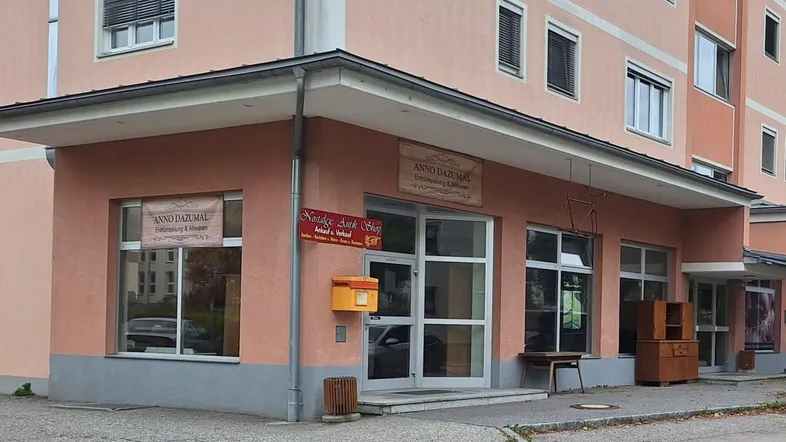Gebäudeansicht mit einem Ladenlokal im Erdgeschoss und Wohnungen darüber, ausgestattet mit Rollläden.
