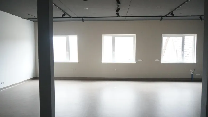 Geräumiger, leerer Raum mit großen Fenstern, Vinylboden und moderner Schienenbeleuchtung.