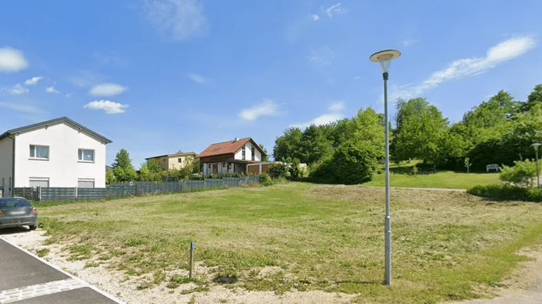 Blick auf ein unbebautes Grundstück in einer Wohngegend mit umliegenden Häusern und viel Grün.