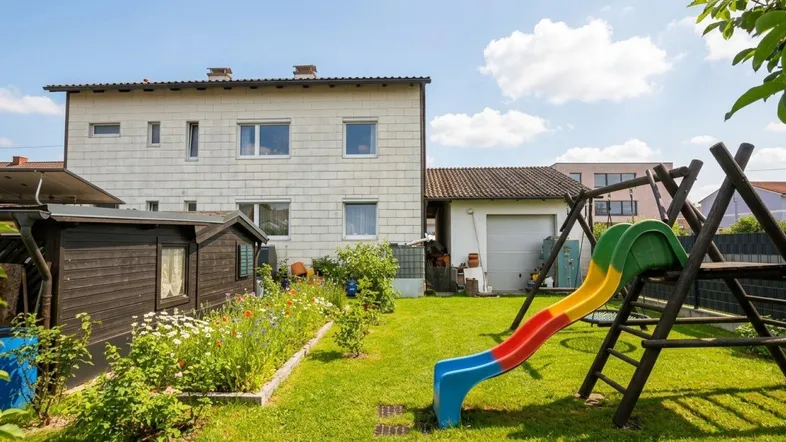 Großer Garten mit Rasenfläche, Blumenbeeten und Kinderspielplatz hinter dem Wohnhaus.
