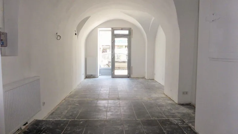 Langer, leerer Raum mit Gewölbedecken und dunklen Fliesen, bereit für die Renovierung.