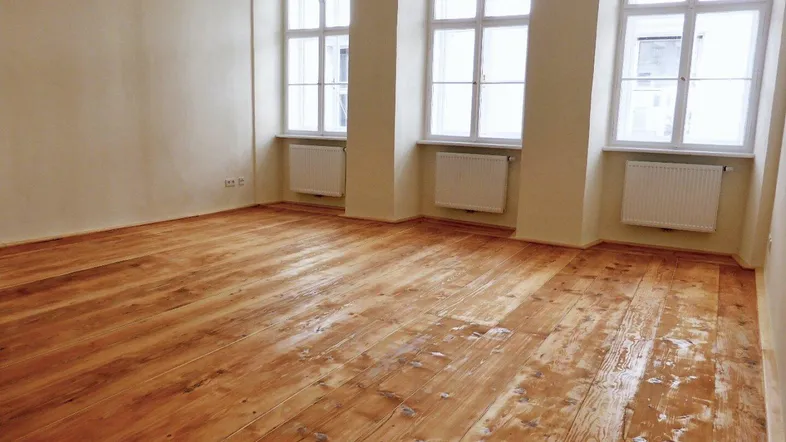 Helles Zimmer mit Dielenboden und drei großen Fenstern, ideal als Wohn- oder Schlafzimmer.
