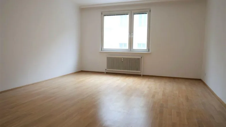 Helles, leeres Zimmer mit Parkettboden und großem Fenster, ideal als Wohn- oder Schlafzimmer.