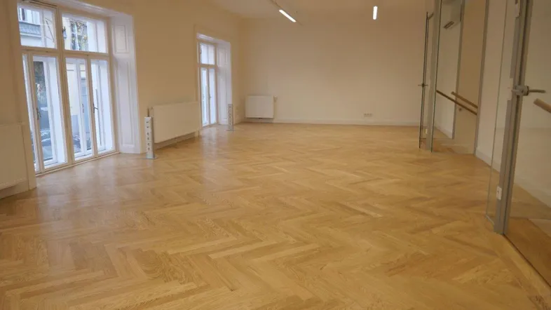 Heller, offener Raum mit Fischgrätparkettboden, großen Fenstern und moderner Beleuchtung.