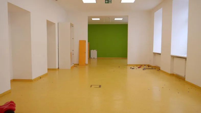 Geräumiger Innenraum mit gelbem Linoleumboden, weißen Wänden und einer grünen Akzentwand, ideal für Kinderaktivitäten.
