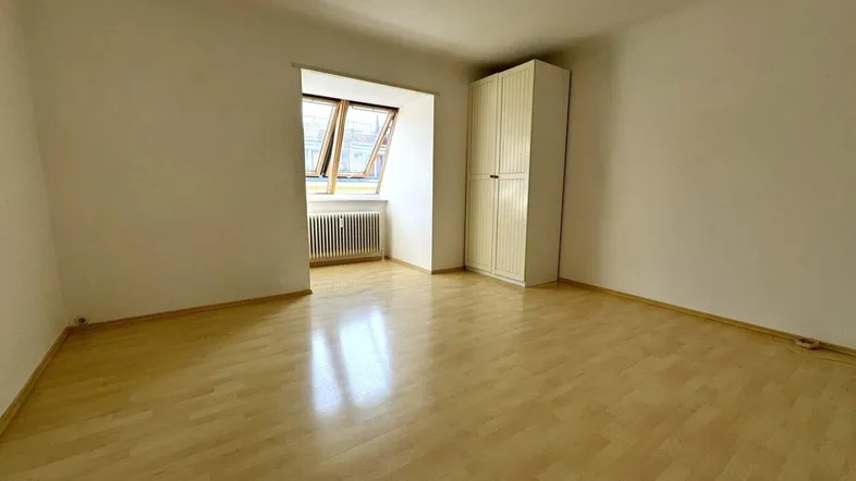 Helles Zimmer mit hellem Laminatboden, weiß gestrichenen Wänden und einem Kleiderschrank.