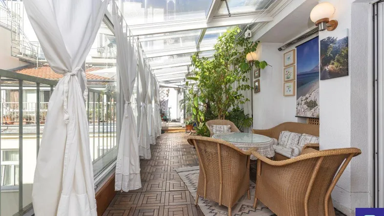 Heller Wintergarten mit Glasdach, Korbmöbeln und vielen Pflanzen, ideal zum Entspannen.