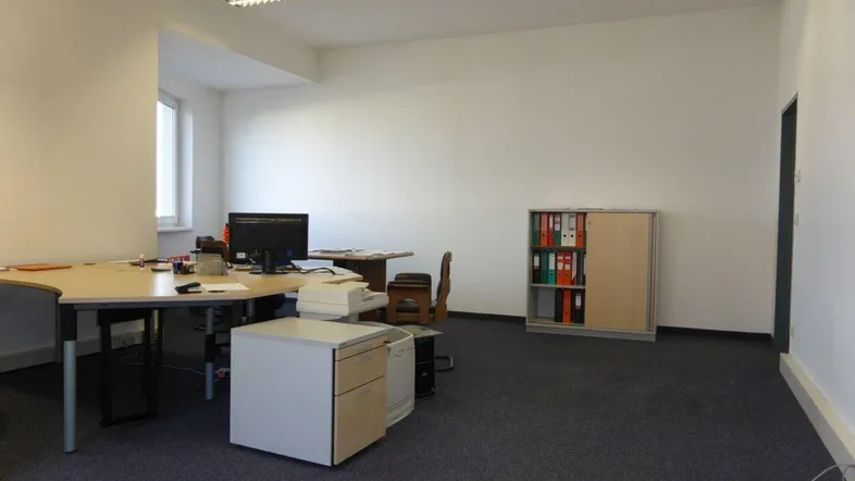 Geräumiges Büro mit Teppichboden, weißen Wänden und funktionaler Einrichtung, ideal für Arbeitsplätze.
