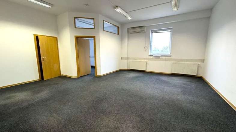 Geräumiges, leeres Büro mit Teppichboden, weißen Wänden und Fenstern, bereit zur individuellen Gestaltung.