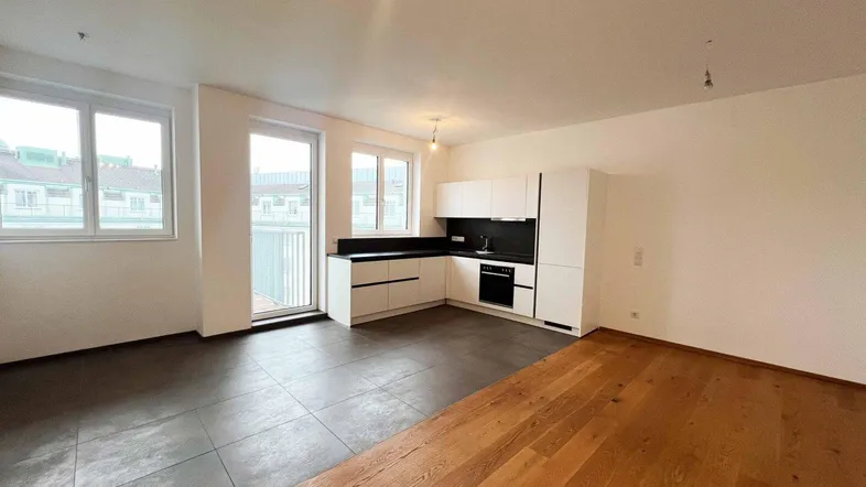 Heller offener Wohn-Essbereich mit moderner Einbauküche, Parkettboden und Zugang zum Balkon.