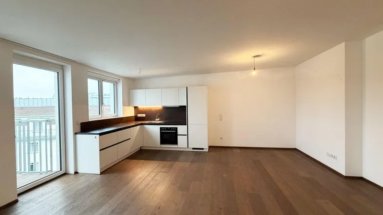 Heller offener Wohnbereich mit integrierter Küche, Parkettboden und Zugang zum Balkon.