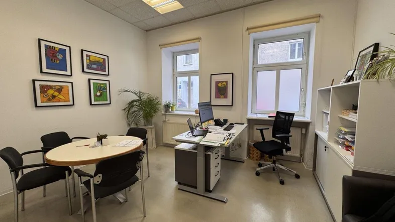 Helles Büro mit zwei Fenstern, Schreibtisch und Besprechungstisch, ideal für produktives Arbeiten in angenehmer Atmosphäre.