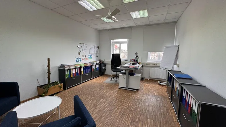 Geräumiges Büro mit Holzparkett, Deckenventilator und mehreren Arbeitsplätzen, ideal für ein Team.