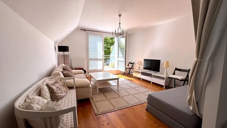 Helles Wohnzimmer mit Holzdielenboden, gemütlicher Sitzecke und Zugang zu einem Außenbereich.