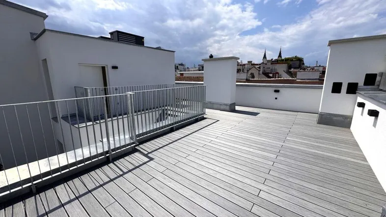 Geräumige Dachterrasse mit Holzboden und weitem Blick über die Stadt unter blauem Himmel.