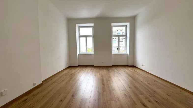 Helles, leeres Zimmer mit neuem Laminatboden und zwei Fenstern, bereit zur individuellen Gestaltung.