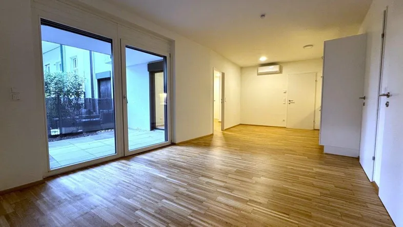 Helles, leeres Wohnzimmer mit Parkettboden und Zugang zu einer Außenterrasse.