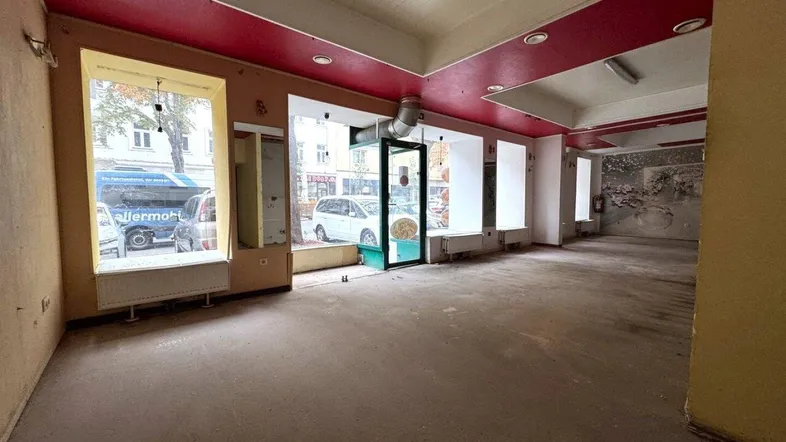 Geräumiger Ladenbereich mit großen Schaufenstern und roter Decke, bereit für Renovierung.