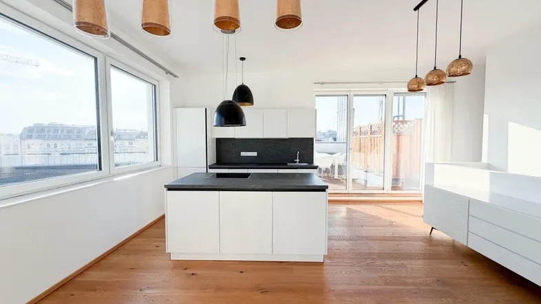 Heller offener Wohnbereich mit moderner Küche, Holzboden und Zugang zu einer Terrasse.