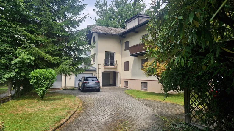 Haus mit gepflasterter Auffahrt, umgeben von hohen Bäumen und gepflegten Grünflächen.