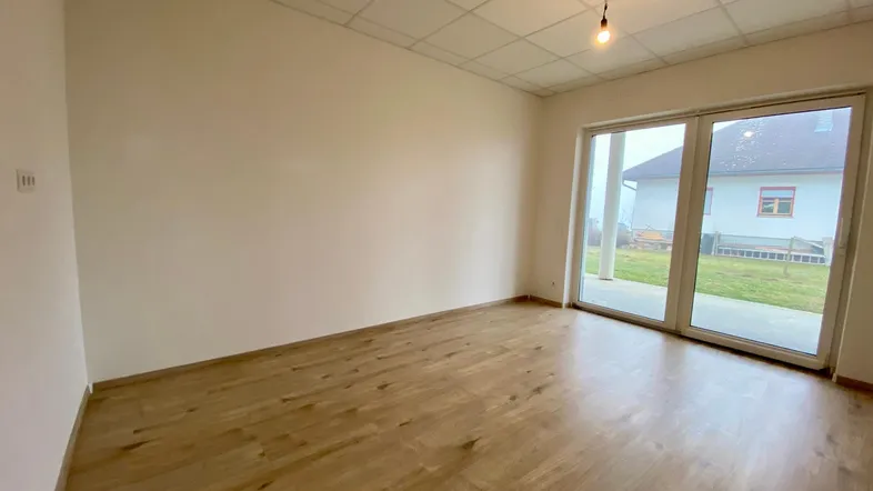 Helles Zimmer mit Holzboden und großen Schiebetüren, die Zugang zum Garten bieten.