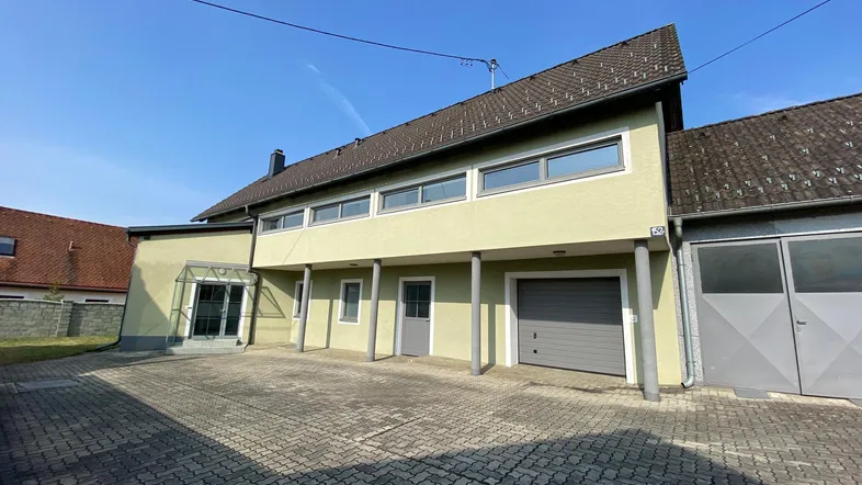 Vorderansicht des Gebäudes mit gepflastertem Vorplatz und Garagentor unter klarem Himmel.