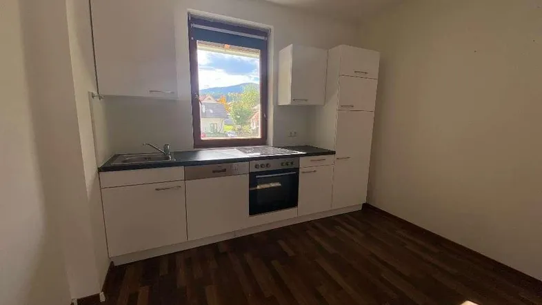 Kleine Einbauküche mit weißen Schränken, dunkler Arbeitsplatte und Fenster mit Blick ins Grüne.