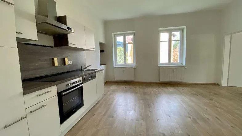 Heller offener Wohn- und Essbereich mit moderner Einbauküche und Laminatboden.