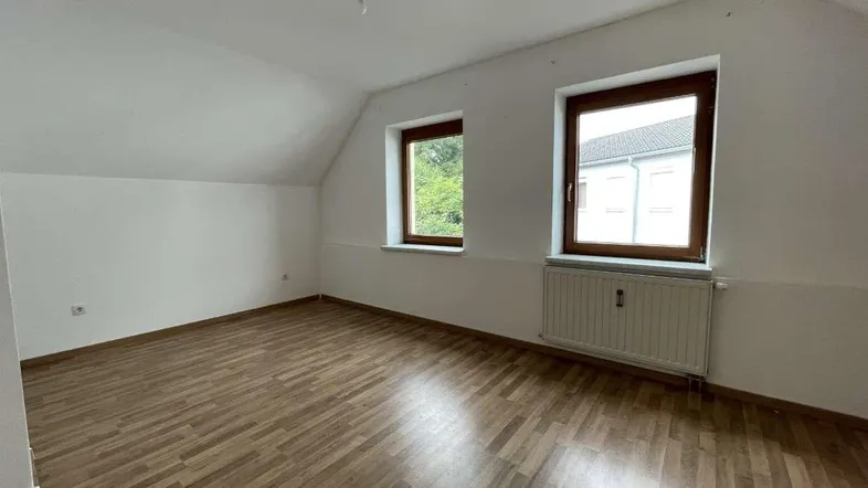 Helles Zimmer im Dachgeschoss mit Schrägen, Laminatboden und zwei Fenstern.