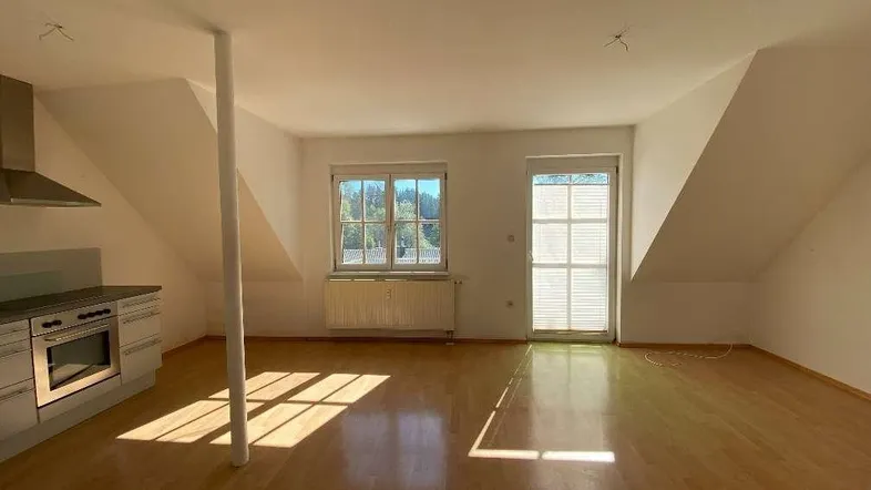 Heller offener Wohn-Essbereich mit integrierter Küche, Dachschrägen und Holzboden.