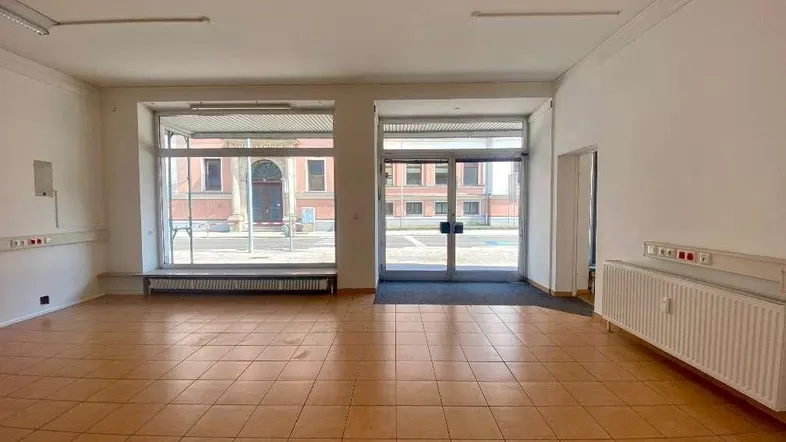 Geräumiger Gewerberaum im Erdgeschoss mit großen Schaufenstern und Fliesenboden, ideal für Ladenlokal.