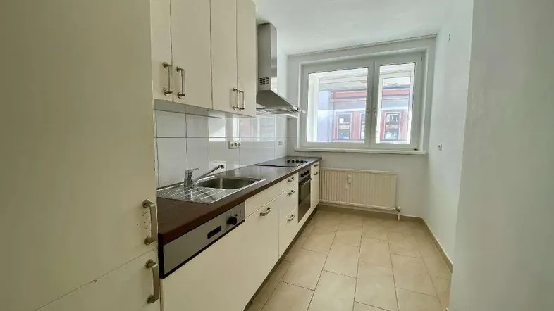 Helle Küche mit Einbauschränken, Fliesenboden und Fensterblick auf die Straße.