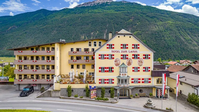 Traditionelles Hotelgebäude mit gelber Fassade und roten Fensterläden vor einer beeindruckenden Bergkulisse.