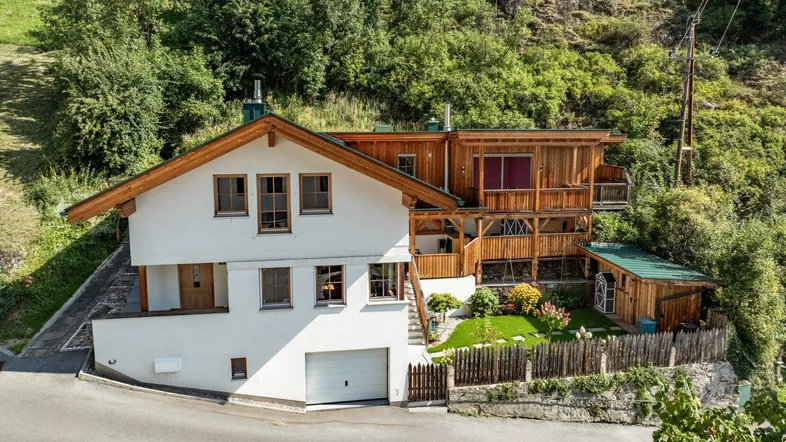 Charmantes Haus im alpinen Stil mit weißer Fassade, Holzverkleidung und integrierter Garage.