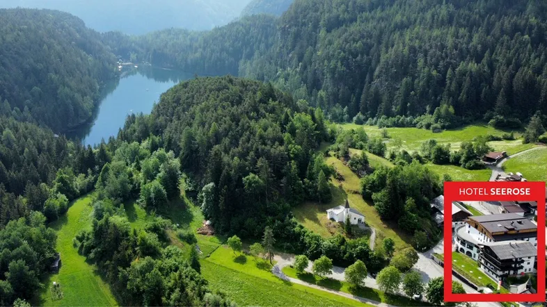 Luftaufnahme einer malerischen Berglandschaft mit See und dichtem Wald, inklusive einer kleinen Ansicht des Hotels.