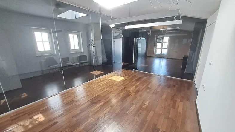 Heller Büroraum mit modernen Glaswänden und elegantem Holzparkettboden, der viel natürliches Licht hereinlässt.
