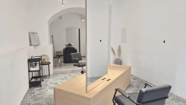 Heller, moderner Friseursalon mit weiß gestrichenen Wänden, gewölbter Decke und großen Spiegeln.