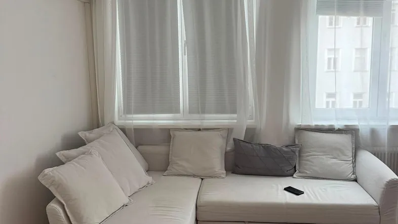 Helles Wohnzimmer mit bequemem Ecksofa, Klimaanlage und dunklem Holzfußboden.