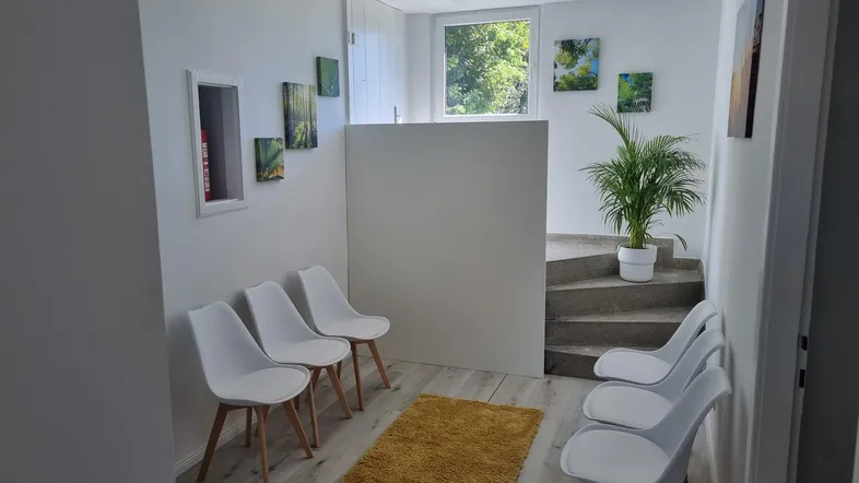 Heller Wartebereich mit modernen weißen Stühlen, Laminatboden und einer Treppe, die in den oberen Bereich führt.