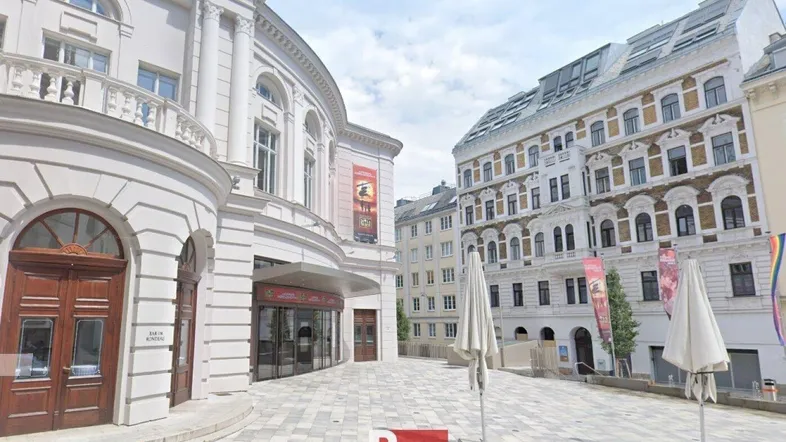 Historisches Gebäude mit eleganter Fassade und gepflastertem Vorplatz in einer städtischen Umgebung.