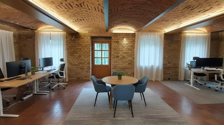 Geräumiges Büro mit freiliegenden Ziegelgewölbedecken, Holzböden und mehreren Arbeitsplätzen.