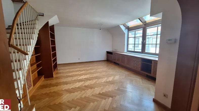 Geräumiger Wohnbereich mit elegantem Fischgrätparkett, Holztreppe und integrierten Schränken unter einem Dachfenster.