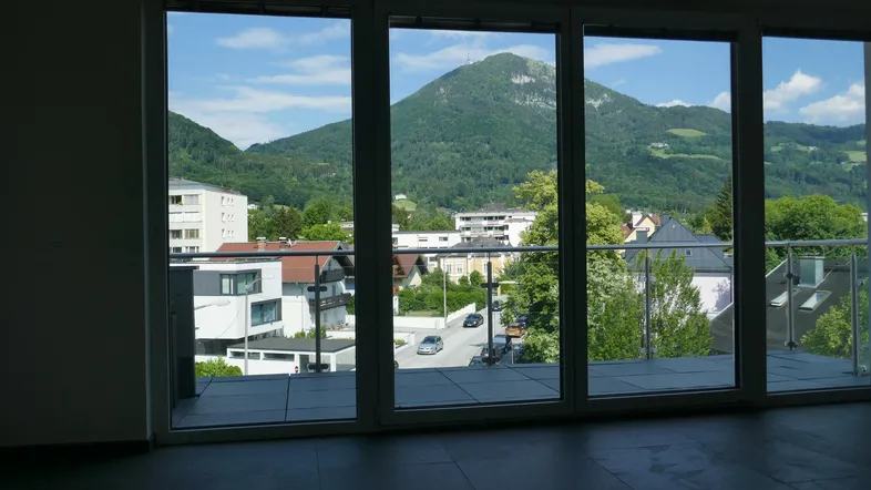 Heller Innenraum mit großen Fenstern und weitem Blick auf die Berge und die Stadt.