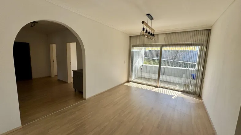 Helles Wohnzimmer mit Parkettboden, Zugang zum Balkon und einem Bogen zu weiteren Räumen.