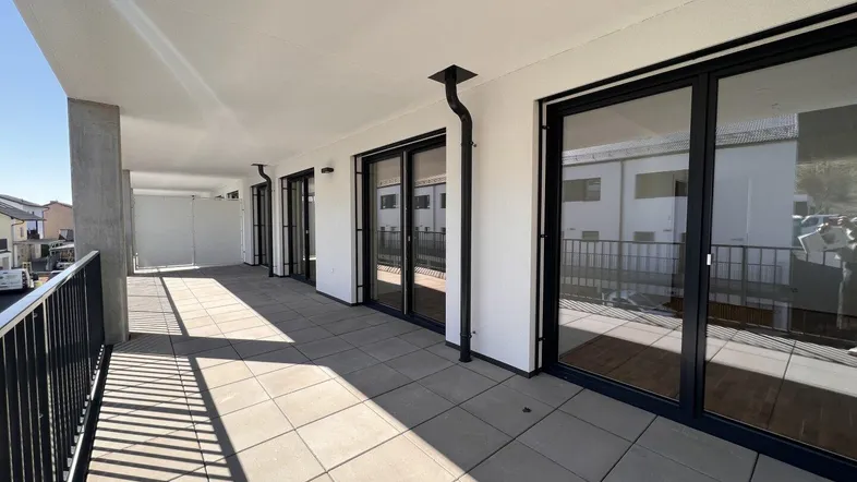 Geräumige, sonnige Terrasse mit Fliesenboden und Zugang zu mehreren Räumen des Gebäudes.