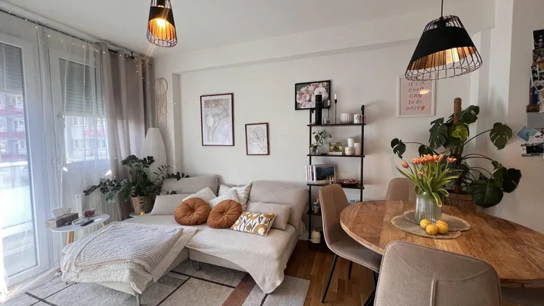 Heller offener Wohn- und Essbereich mit Holzboden, modernen Möbeln und Zugang zum Balkon.