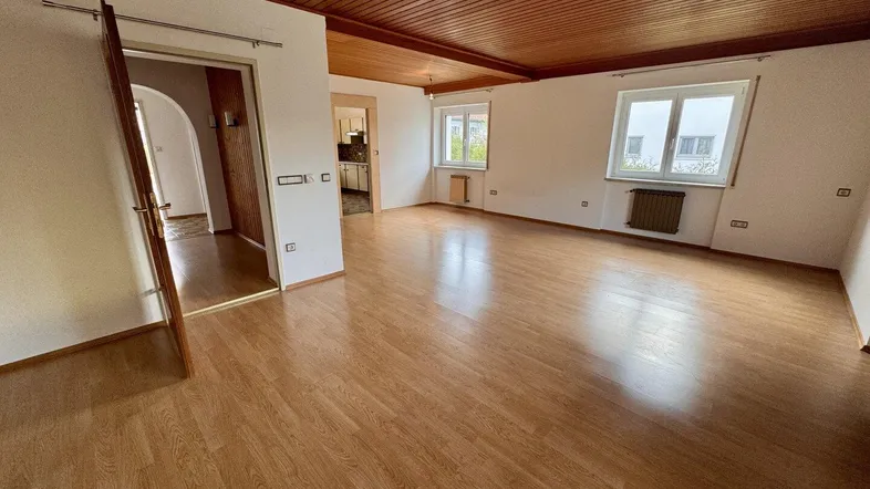 Geräumiges Wohnzimmer mit hellem Laminatboden und Holzdeckenverkleidung, bietet viel natürliches Licht.