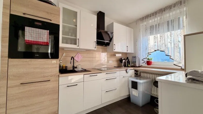Moderne Küche mit weißen Hochglanzfronten, Holzakzenten und Fenster für natürliches Licht.